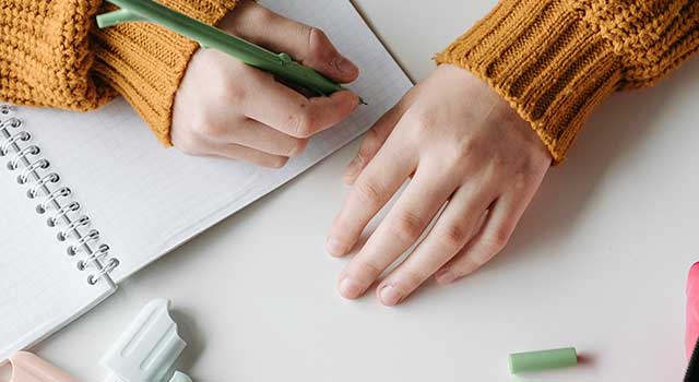 Student writing in a notebook with pencils, representing writing contests for kids and teens.
