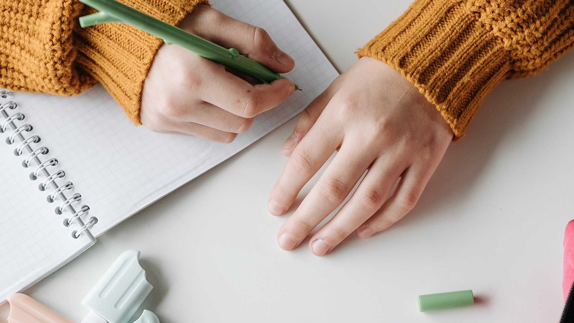 Student writing in a notebook with pencils, representing writing contests for kids and teens.